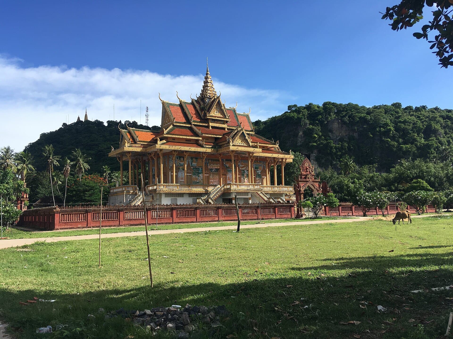 The golden temple of Wat Phnom Sampeau standing in open grass below the limestone cliffs of the hill outside Battambang