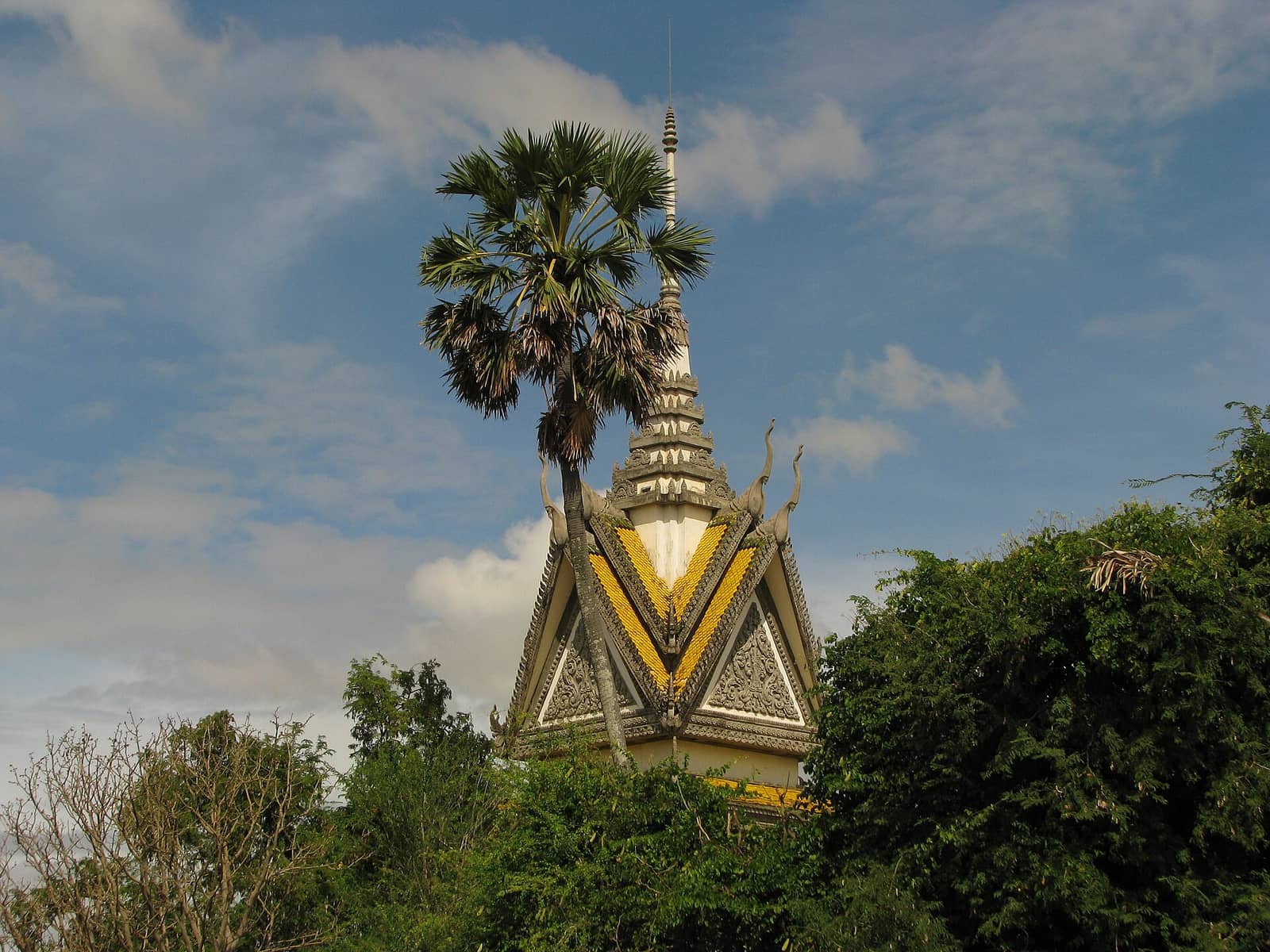 The white and gold memorial stupa at Choeung Ek rising above the treeline against an open sky
