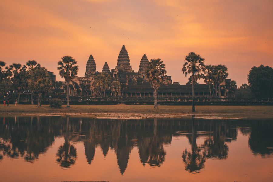 Angkor Wat silhouetted against an orange dawn sky and reflected in the lake in front of it