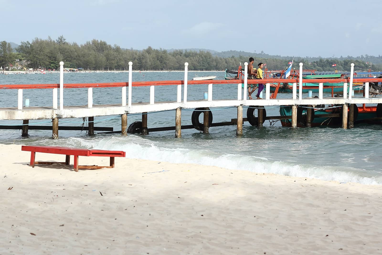 A red-railed jetty running out from the sand at Ochheuteal Beach with fishing boats moored along it